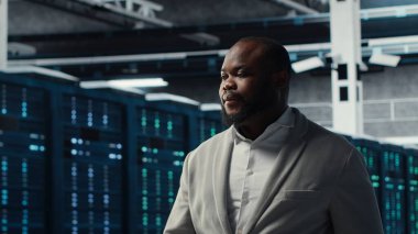 Sunucu merkezindeki gülümseyen mühendis veri merkezinin enerji tüketimini bileşenler arasında izliyor. Veri merkezinde yürüyen mutlu bilişim uzmanı, sondaj sensörlerinin en uygun şekilde çalıştığından emin oluyor.