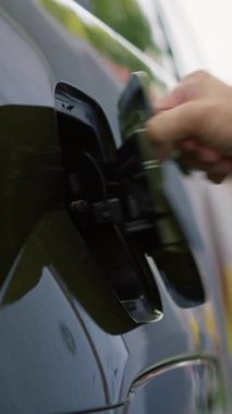 Dikey video. Elektrikli motora güç veren aküyü şarj etmek için elektrikli araç kapağını açan sürücüyü kapat. Kişi, aküyü şarj etmek için EV otomobilinin giriş portunu fişe takarak açar