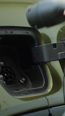 Sürücünün EV araç aküsüne elektrik kablosu bağlarken ki dikey videosunu kapat. EV otomobil giriş portunu açan kişi, aküyü eko 'ya bağlayarak şarj etmek için açar
