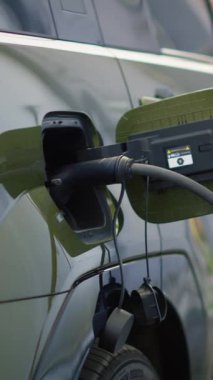 Modern istasyonda elektrikli SUV 'nin şarj olurken çekilen dikey video temiz enerji taşımacılığını gösteriyor. EV prizi elektrikli arabaya bağlı, çevre dostu teknoloji kavramı
