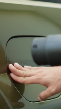 Eko-bilinçli sürücünün, yenilenebilir enerji taşımacılığına geçişi desteklemek amacıyla, şarj edilecek elektrikli arabanın iskele kapağını açtığı dikey video. Adam elektrik kablosu bağlayıcısı yerleştiriyor