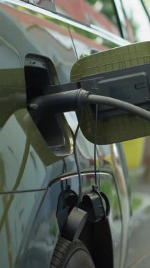 Dikey video çevre dostu elektrikli araba aküsü şarj ediliyor, alternatif enerji taşımacılığına geçiş kavramı. EV aracına bağlı elektrik kablosu bağlantısı yükleniyor, el bilgisayarı