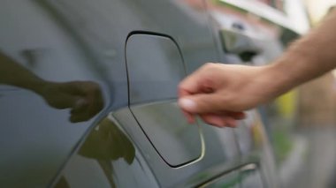 Kişi, park halindeyken şarj etmek için EV çevre dostu aracın giriş kapağını açar. Sürücü şarj edilebilir pille donatılmış elektrikli aracın şarj kapağını açar