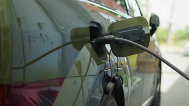 Çevre dostu elektrikli araba aküsü şarj ediliyor, alternatif enerji taşımacılığına geçiş kavramı. EV aracına bağlı elektrik kablosu bağlantısı şarj ediliyor, el kamerası görüntüsü