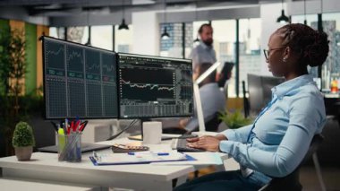 Komisyon şirketindeki portföy yöneticisi hisse senedi piyasası eğilimlerini analiz ederek getirileri artırıyor. Afrikalı Amerikalı kadın yatırım fırsatlarını belirlemek için borsa ölçümlerini takip ediyor, kamera A