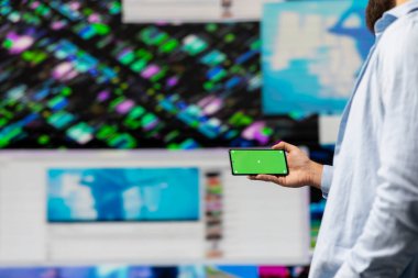 Genç adam telefondaki yeşil ekrana kullanıcı arayüzü olarak bakıyor, sosyal platformlarda online varlığı kontrol ediyor. Dijital dünyada yaratıcılık ve çevrimiçi ilişki üzerine çalışan erkek nüfuzu.