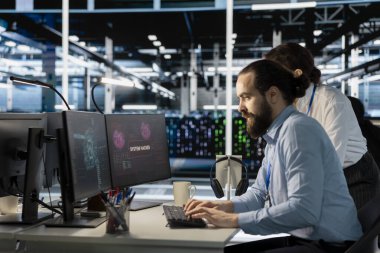 Veri merkezindeki mühendisler PC monitöründen fidye yazılımı uyarısına tepki göstererek kritik sistemleri korumak için protokolü başlatıyorlar. Bilgi işlem uzmanları hackleme girişimlerini gözden geçirir ve altyapının zarar görmesini değerlendirir