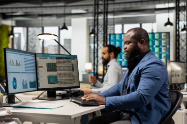Afrikalı Amerikalı iş adamı performans ölçüm ve grafiklerini analiz ediyor, yönetim stratejisini optimize etmek ve kurumsal büyüme, yenilik ve başarıyı güvence altına almak için iş raporları hazırlıyor.