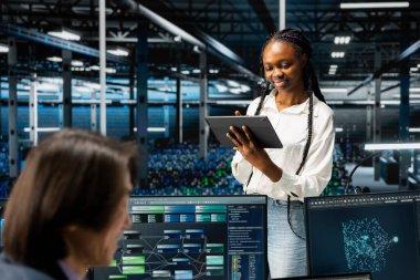 Gülümseyen veri merkezi yazılım geliştiricisi, tablet, kodlama, yönetim sistemlerini kullanıyordu. Sunucu merkezinde programlama dili kullanan meslektaşlarının yanında mutlu bilişim uzmanı