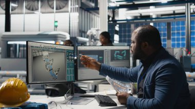 Siyahi alternatif enerji danışmanı bir güneş enerjisi santralinde faaliyet göstererek, fabrika uygulamalarının yeşil enerji hedeflerine ulaşmasını sağlıyor. Uzman, verimlilik üretmek için bilgisayar kullanıyor. Kamera A.