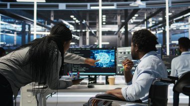 Tekerlekli sandalyedeki veri merkezi mühendisi ve meslektaşı düğüm ağacı programlama aracı kullanarak otomatik görevleri denetliyor. Özel sunucu tarım ekibi, AI analizlerine ve kamera A 'ya dayalı sistem ayarlarını ayarlar