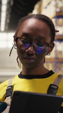 Tabletteki depo yönetim sistemindeki kayıtları güncellemek ve sipariş işlemlerini sağlamak için nakliye etiketlerini tarayan dikey video kadın çalışanları. Depolarda e-ticaret dağıtım işlemleri yap