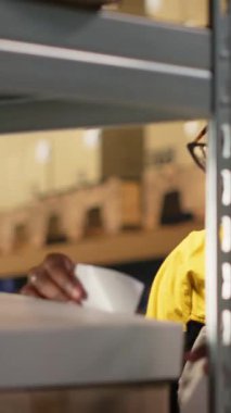 Dikey Video Siyah kadın işçi paketlere yapışkan havayolu fatura etiketleri uyguluyor, sevkiyat detayları ve izleme bilgileriyle dağıtım için ürünleri hazırlıyor. Depo 'da endüstriyel işlemler