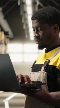 Dikey Video Siyah erkek personel e-ticaret lojistik merkezinde envanter paletleri doğruladı. Dizüstü bilgisayarda doğru işlem ve büyük ölçekli depo ayarlarında hızlı nakliyat için ambalaj