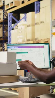 Dikey Video İşçisi etiketleri uyguluyor ve barkod etiketlerindeki takip bilgi numaralarını tarıyor, karton kutulara nakliye etiketleri kaydediyor. Tamamlama Merkezi personeli paket durumu ve teslimatı gösteriyor