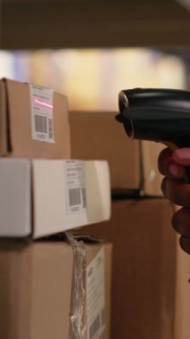 Dikey Video Siyah kadın çalışanı tarayıcı kullanarak envanterdeki hava yolu faturalarını kontrol ediyor, endüstriyel depodaki lojistik operasyonları çözüyor. Rafların yakınındaki nakliye etiketlerini doğrulayan işçiler