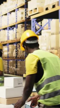 Dikey Video Depolama odası çalışanı envanterde kayıt yapmak için nakliye etiketlerini tarıyor, depo yönetim sistemindeki kayıtları güncelliyor. Sanayi bölgesinde e-ticaret dağıtım işlemleri