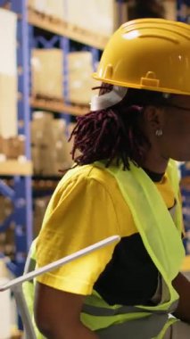 Dikey Video Siyah çalışanları kalabalık depo ortamında paket sevkiyatı takım çalışmasından gurur ve memnuniyet duyarak bir beşlik jest paylaşıyorlar. Verimliliği sağlamak için görevler zamanında bitiriliyor