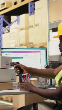 Dikey Afrikalı Amerikalı katip, büyük sanayi raflarındaki kutuların sevkiyat detaylarını kaydetmek için barkod tarayıcısı kullanıyor. Paket izleme servisi için havayolu faturaları taranıyor, doğru lojistik