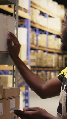 Endüstriyel depo kutularına yapışkan nakliye etiketleri uygulayan dikey video erkek personel üyesi, sorunsuz ekspres dağıtım ve sipariş işleme emin olmak için yanlış takip numaraları içeren paketleri etiketleme