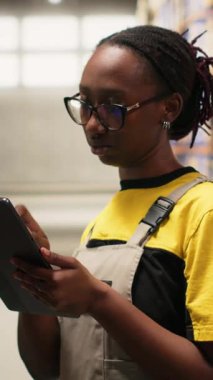 Tabletle ve dağıtım merkeziyle birlikte sipariş işleme görevlerinde çalışan dikey Video Siyah kadın endüstriyel katip verimli bir depolama operasyonu sağlıyor. E-ticaret iletimi için veri paketlerini yönetir