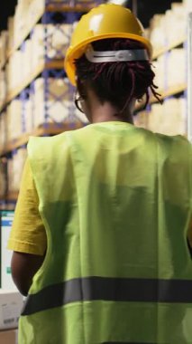 Vertical Video Afrikalı Amerikalı depo görevlisi paket güzergahını denetliyor. Bilgisayar yazılımlarındaki izleme bilgilerini güncelliyor.