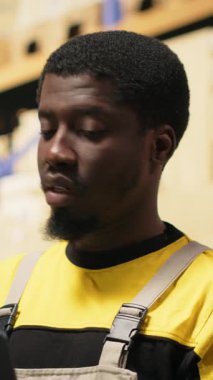 Dikey Video Afrikalı Amerikalı erkek personel, yoğun depolama merkezindeki ambalajları düzenliyor. Raflarda dizüstü bilgisayarla ve ürünlerle envanter tutuyordum. E-ticaret düzeni işleme