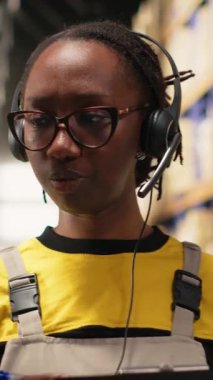 Dikey Video Çağrı Merkezi kadın çalışanı bir depo deposunda müşterilere yardım ediyor, paketlerdeki ve raf ünitelerindeki etiketleri kontrol ediyor. Doğumla ilgili sorunları ve gecikmeleri çözen genç yetişkinler