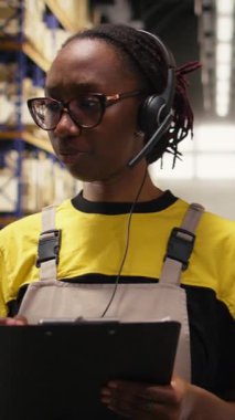 Dikey Video Çağrı Merkezi kadın çalışanı bir depo deposunda müşterilere yardım ediyor, paketlerdeki ve raf ünitelerindeki etiketleri kontrol ediyor. Doğumla ilgili sorunları ve gecikmeleri çözen genç yetişkinler