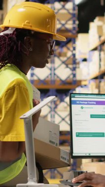 Dikey Video Deposu operasyon ekibi gelen malları yönetiyor, kargo taşıma detayları için bilgisayardaki izleme yazılımını takip ediyor. Dağıtım merkezinde yüksek yelekli çalışanlar