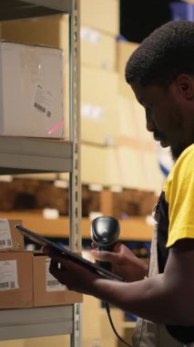 Vertical Video Fulfillment Center çalışanı envanterde kayıt yapmak için nakliye etiketlerini tarıyor, yönetim sistemindeki kayıtları tablet üzerinde güncelliyor. Sanayi bölgesinde e-ticaret perakende dağıtım operasyonları