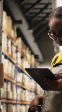 Dikey Video Siyah Kadın çalışanları, ambardaki kutuların etiketlerini işlemek için barkod tarayıcısı kullanıyorlar. İz sürme bilgisi ve doğru lojistik ile paket izleme servisi için yanlış etiketler taranıyor