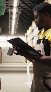 Dikey Video Personel Üyesi endüstriyel depo kutularına yapışkan nakliye etiketleri yapıştırıyor, paketleri yanlış takip numaralarıyla etiketliyor ve sorunsuz ekspres dağıtım ve sipariş işlemlerini sağlama alıyor. Kamera.