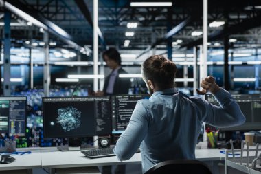 Veri merkezi mühendisi, bakım için AI LLM asistanını kullanırken yorgunluğu azaltmak için çalışma istasyonunda esneme hareketleri yapıyor. Sunucu merkezi çalışanı bilgisayarın başında uzun saatler geçirdikten sonra rahatlıyor