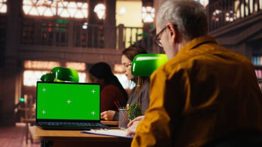 Akademik materyalleri yeşil ekranla inceleyen son sınıf öğrencisi, sınavlar ve tez tamamlama için önemli bilgiler topluyor. Yaşlı adam üniversiteden mezun olma konusunda ciddi..