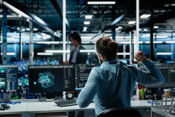 Veri merkezi mühendisi, bakım için AI LLM asistanını kullanırken yorgunluğu azaltmak için çalışma istasyonunda esneme hareketleri yapıyor. Sunucu merkezi çalışanı bilgisayarın başında uzun saatler geçirdikten sonra rahatlıyor