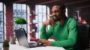 Afrikalı Amerikalı uzaktan kumandalı işçi evde online araştırma yapıyor, önemli verileri yazıyor ve topluyor. Teleworker, evdeki günlük ödev ve makaleleri okumaya odaklandı. Kamera B.