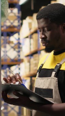 Dikey Video Personel Üyesi endüstriyel depo kutularına yapışkan nakliye etiketleri yapıştırıyor, paketleri yanlış takip numaralarıyla etiketliyor ve sorunsuz ekspres dağıtım ve sipariş işlemlerini sağlama alıyor. Kamera.