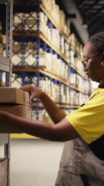 İthalat işlemi sırasında kargo detaylarını doğrulayan siyah kadın işçilerin dikey video portresi. Dağıtımda güvenlik önlüğü giymek ve pürüzsüz takip sayıları lojistiği kayıtları yönetmek