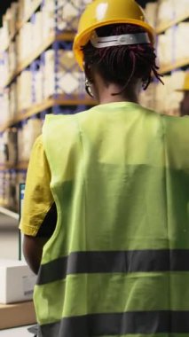 Lojistik merkezde çalışan dikey Afrikalı Amerikalı kadın bilgisayarla ilgili bilgileri takip ediyor, teslimat güzergahını ve diğer sevkiyat detaylarını gerçek zamanlı olarak güncelliyor. Çevrimiçi siparişler için paket durumu takip ediliyor