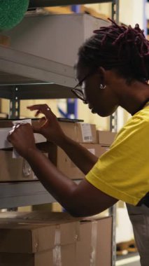 Dikey Video Deposu kâtibi depo deposundaki kutulara yapışkan nakliye etiketleri yapıştırıyor, paketleri yanlış takip numaralarıyla etiketliyor ve kusursuz ekspres teslimat ve sipariş işlemlerini sağlama alıyor.