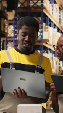 Lojistik merkezindeki sipariş işlemleri için dizüstü bilgisayardaki paket verilerini ele alan Dikey Video Siyah ekip üyeleri, dağıtım protokolleri için palet gönderme etiketlerini doğruladılar. Verimli bir e-ticaret deposu