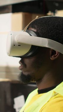 Dikey video depo memuru sanal gerçeklik kulaklığını online alışveriş siparişleri için kullanıyor, envanterden kargo malları hazırlıyor ve bilgisayar yazılımındaki paket durumunu izliyor. İşlem emri. Kamera.