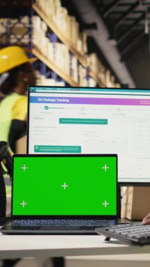 İthalat ihracat detaylarıyla ilgilenen dikey video çalışanı. Ekranda kopyalama alanı var. Depo masasında güvenlik yeleği ve kask takıyor. Personel izleme paketi yazılım takibi. Kamera.