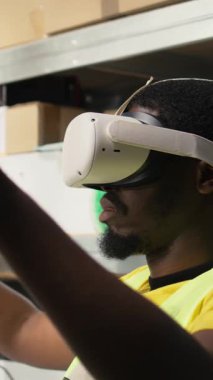 Dikey video depo memuru sanal gerçeklik kulaklığını online alışveriş siparişleri için kullanıyor, envanterden kargo malları hazırlıyor ve bilgisayar yazılımındaki paket durumunu izliyor. İşlem emri. Kamera.