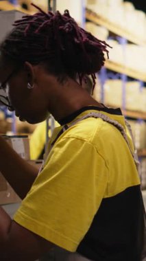 Dikey Video Afrikalı Amerikalı çalışan kargo etiketlerini dağıtım merkezindeki kargo kutularına yapıştırıyor, envanter ve sipariş işlemlerini awb çıkartmalarıyla yapıyor. Çevrimiçi alışveriş büyük iş