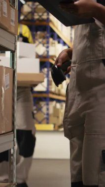 Dikey Video Afrikalı Amerikan e-ticaret işçisi nakliye etiketlerinin numaralarını tarıyor, envanter kayıtları için bavul ve sevkiyat detaylarını kaydediyor. Palet dağıtım işlemleriyle ilgilenen genç adam