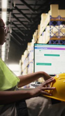 Dikey Video Siyah depo yöneticisi personeli için hayal kırıklığını ifade ediyor, sipariş gecikmelerini çözmek için paket izleme yazılımlarını kontrol ediyor. Dağıtım merkezinde baskı altında çalışan genç adam.