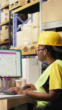 Dikey Video Deposu siyah işçisi dijital sevkiyat durumunu inceliyor, takip yazılımında yanlış numaralar kullanıyor. Depoda veri güdümlü sipariş takip ve teslimat güncellemeleri yapan kadın. Kamera A.