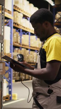 Vertical Video Fulfillment Center çalışanı envanterde kayıt yapmak için nakliye etiketlerini tarıyor, yönetim sistemindeki kayıtları tablet üzerinde güncelliyor. Sanayi bölgesinde e-ticaret perakende dağıtım operasyonları